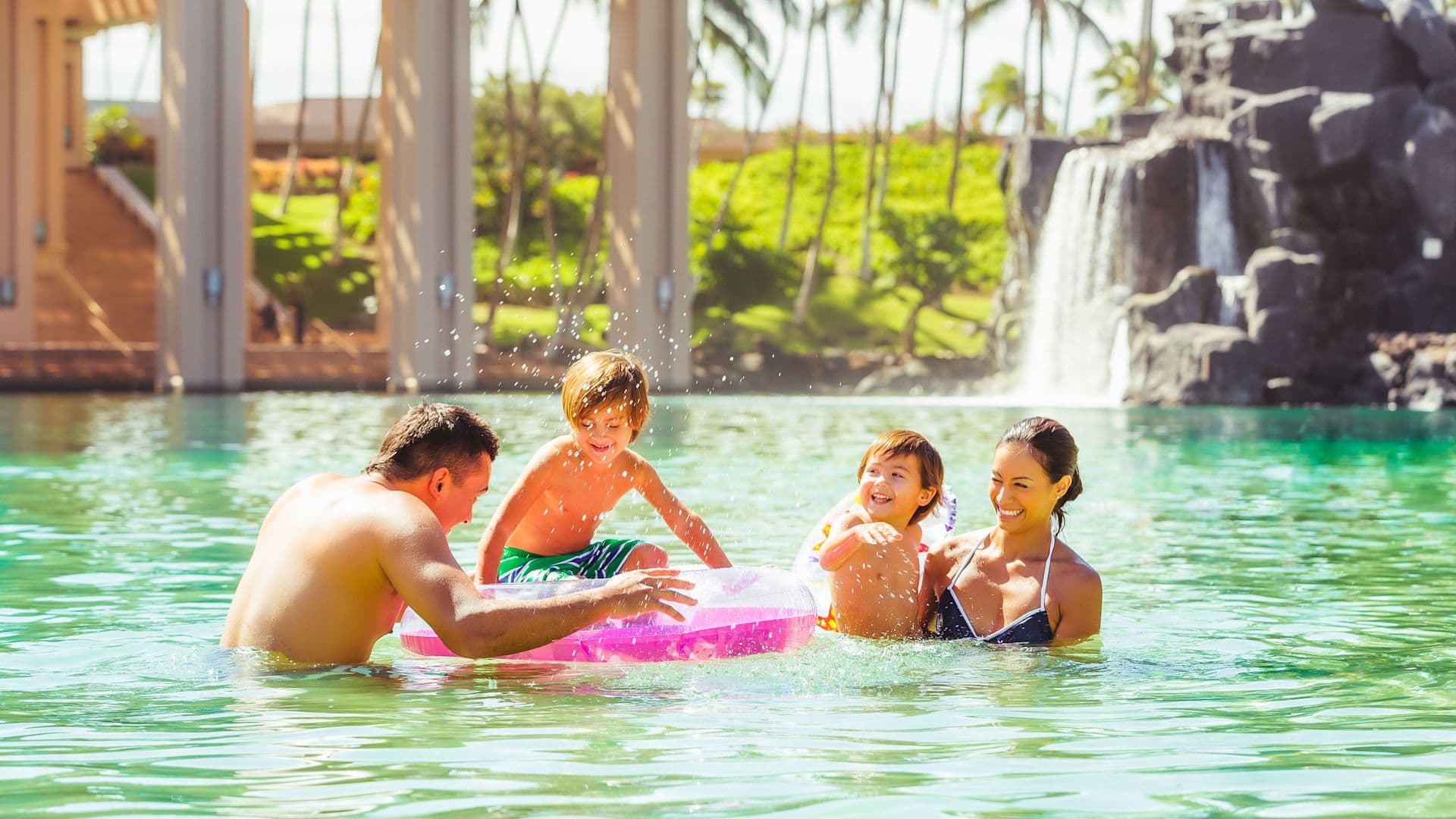 A family of four in a resort pool splashing each other.