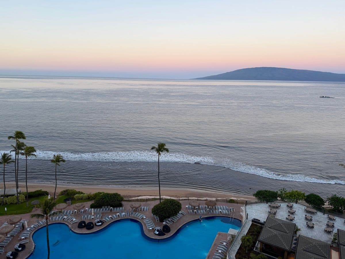 Sunrise view over a pool and ocean looking out hotel room window at Hyatt Maui in Hawaii.