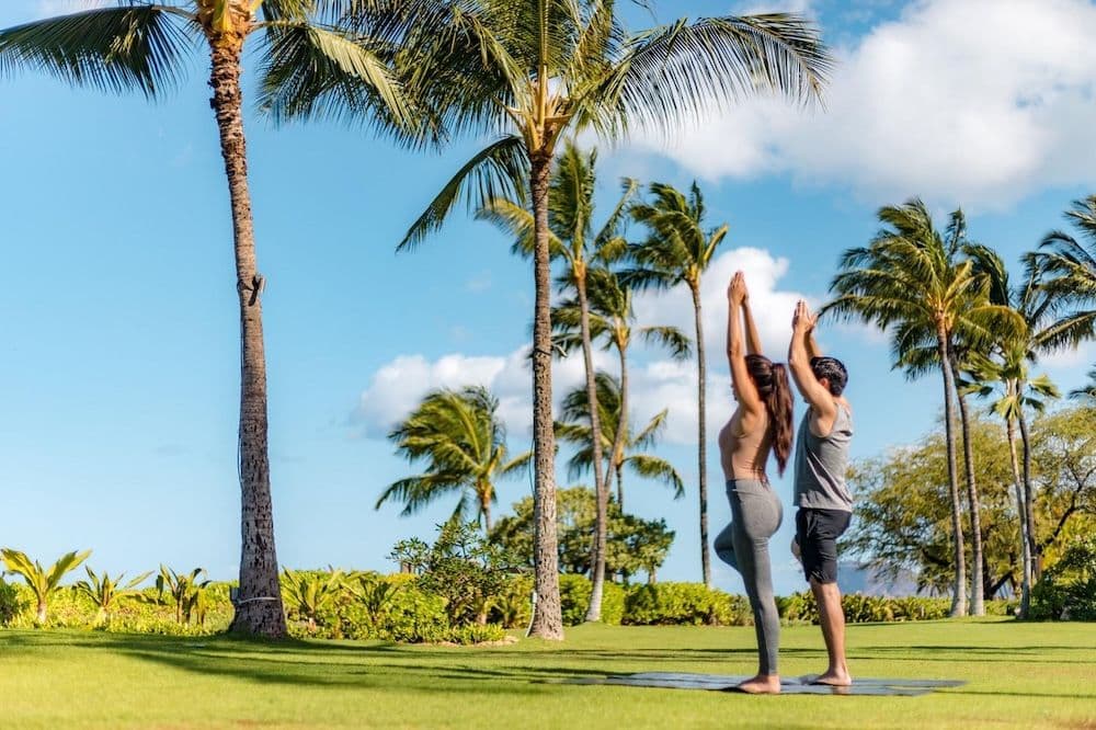 A couple doing outdoor yoga in Hawaii with palm trees.