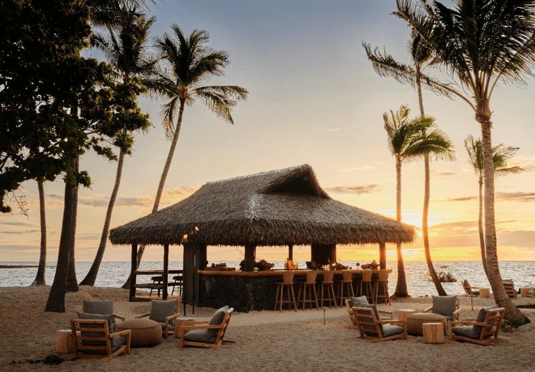 A thatched roof bar on the beach with palm trees and lounge chairs