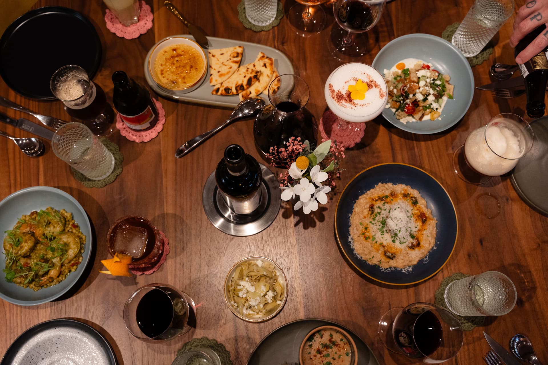 A birdseye image of a dining room table filled with food, cocktails and flowers
