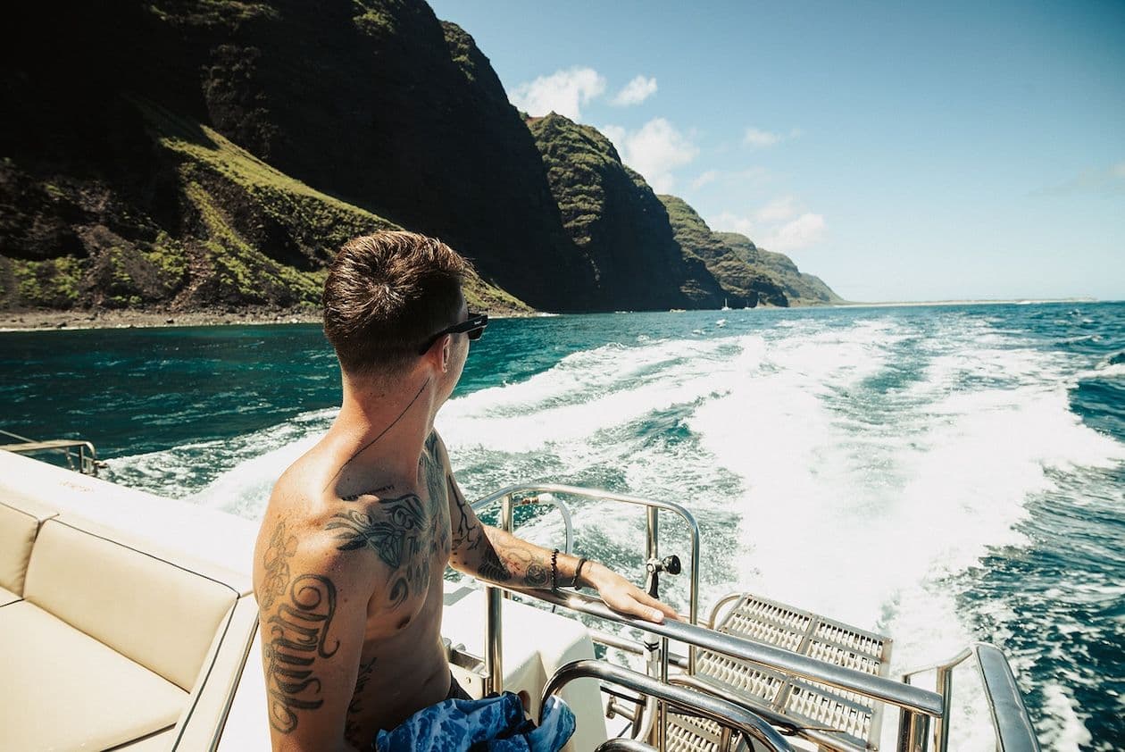 Man looking off the back of a boat next to the Napali Coast in Kauai.