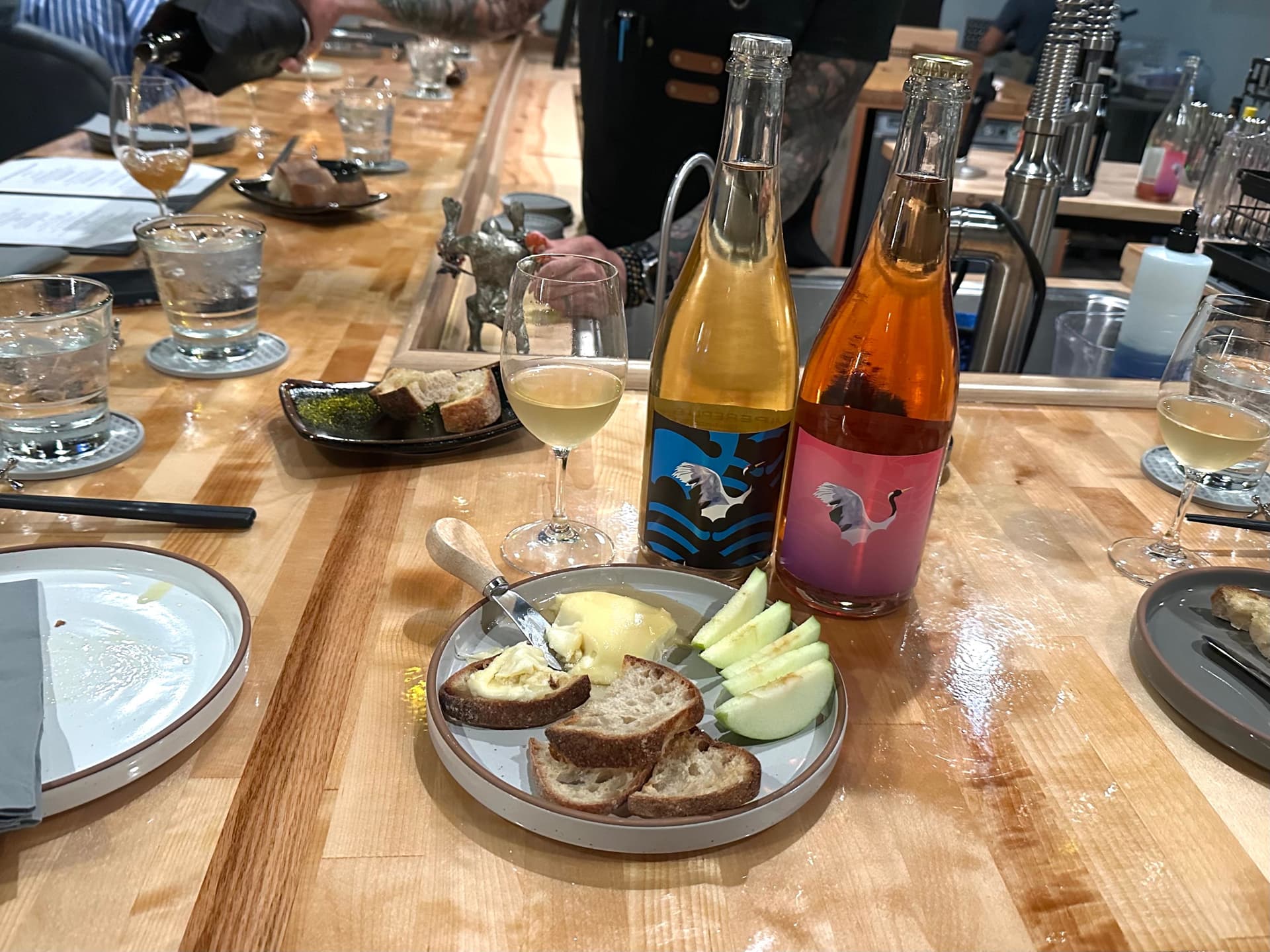 A bar with wine bottles, glasses and cheese with bread and apple slices.