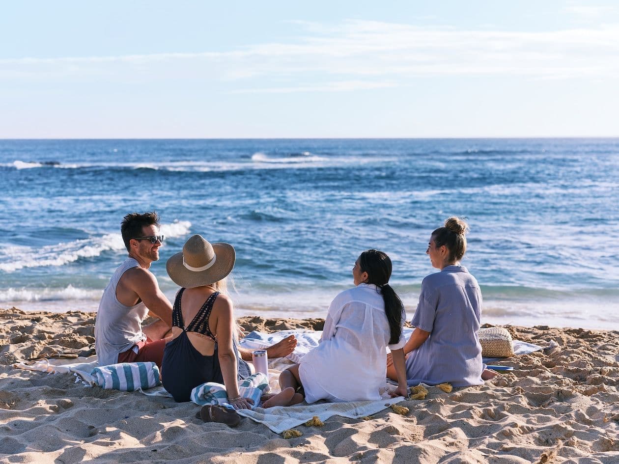 Four friends sitting on the sand at poipu beach on Kauai.