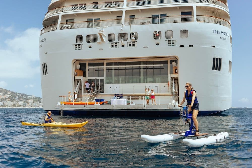 A man kayaking and woman floating in the ocean by a cruise ship.