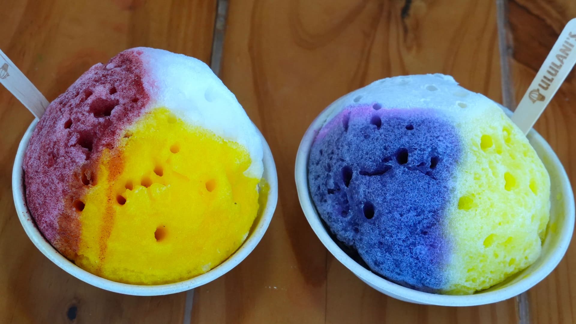 Two cups of shave ice in rainbow colors.