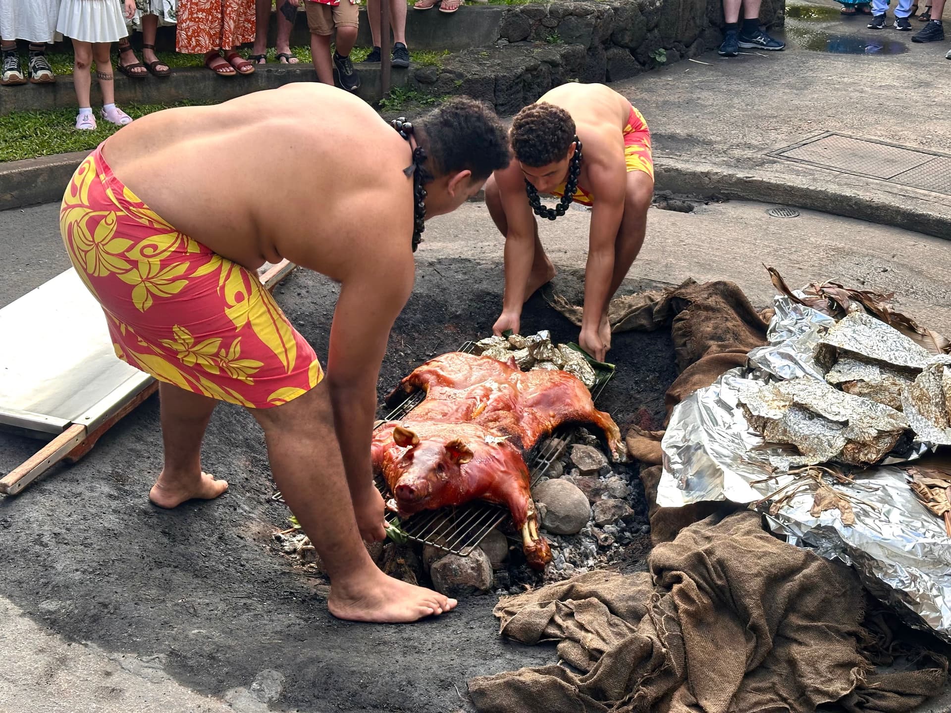 two men pulling a whole pig out of an imu