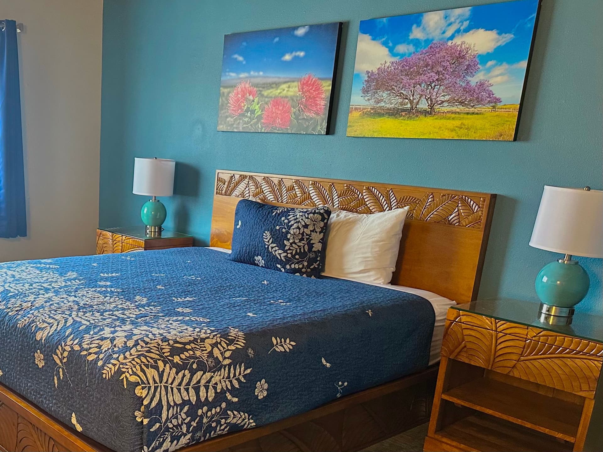 Hotel bedroom with blue bedspread and wood bed frame, art on walls