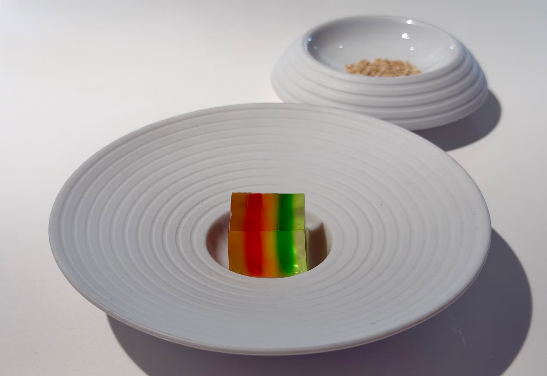 A rainbow piece of jello in a large white plate.