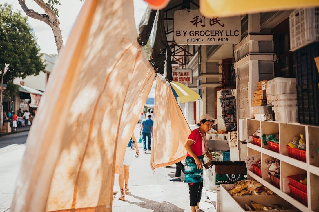 A woman outside her produce market in chinatown honoluu hawaii.
