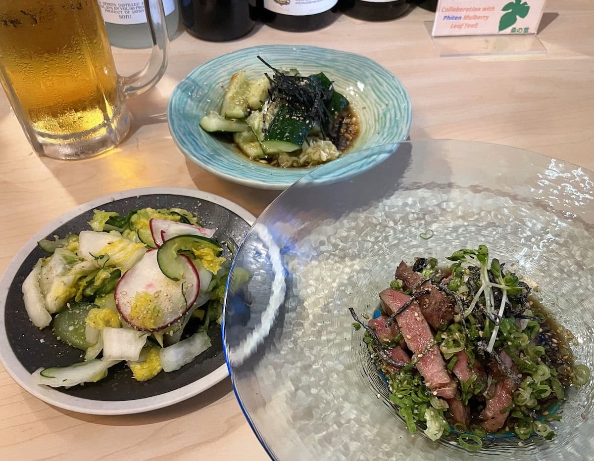 plates of japanese food on a table with a mug of beer