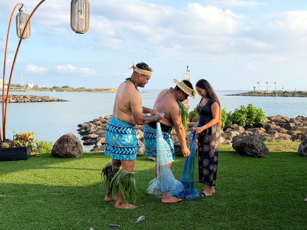 Two men showing a woman how to throw net. One of the cultural activities at Kaula Lūʻau on oahu hawaii