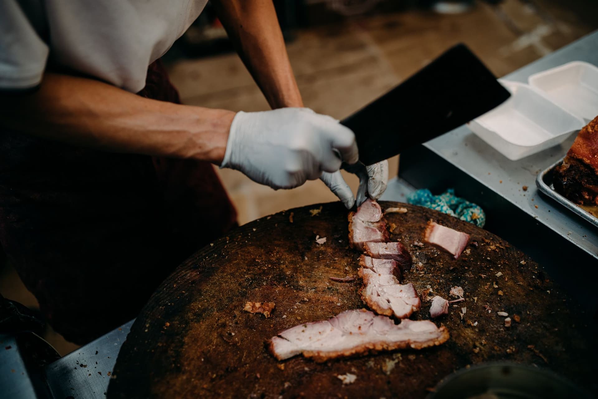 A man chopping roast pork on a butcher block with a large cleaver in Chinatown, Honolulu.