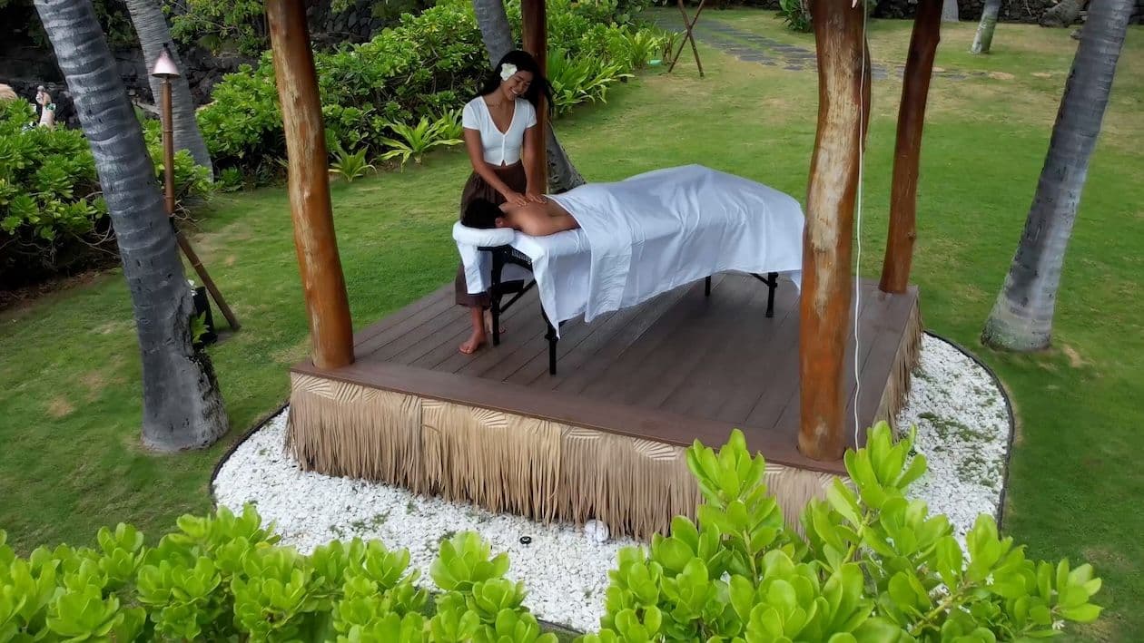 A woman giving a man a massage at the open air The Lotus Center Spa at royal kona resort on big island, hawaii.